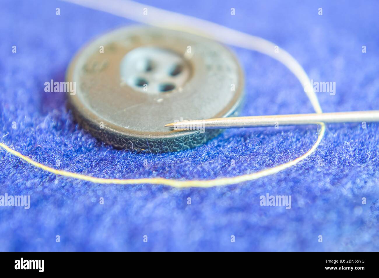 Un fil à aiguille et un bouton conservés sur une nappe bleue illustrant l'artisanat, l'art fait maison Banque D'Images