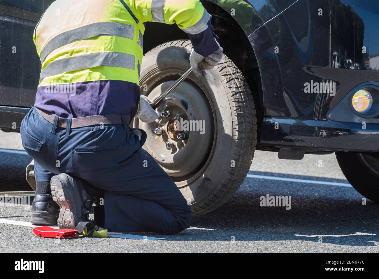 Un mécanicien qui change la vieille roue d'une voiture sur la route pour obtenir de l'aide. Banque D'Images