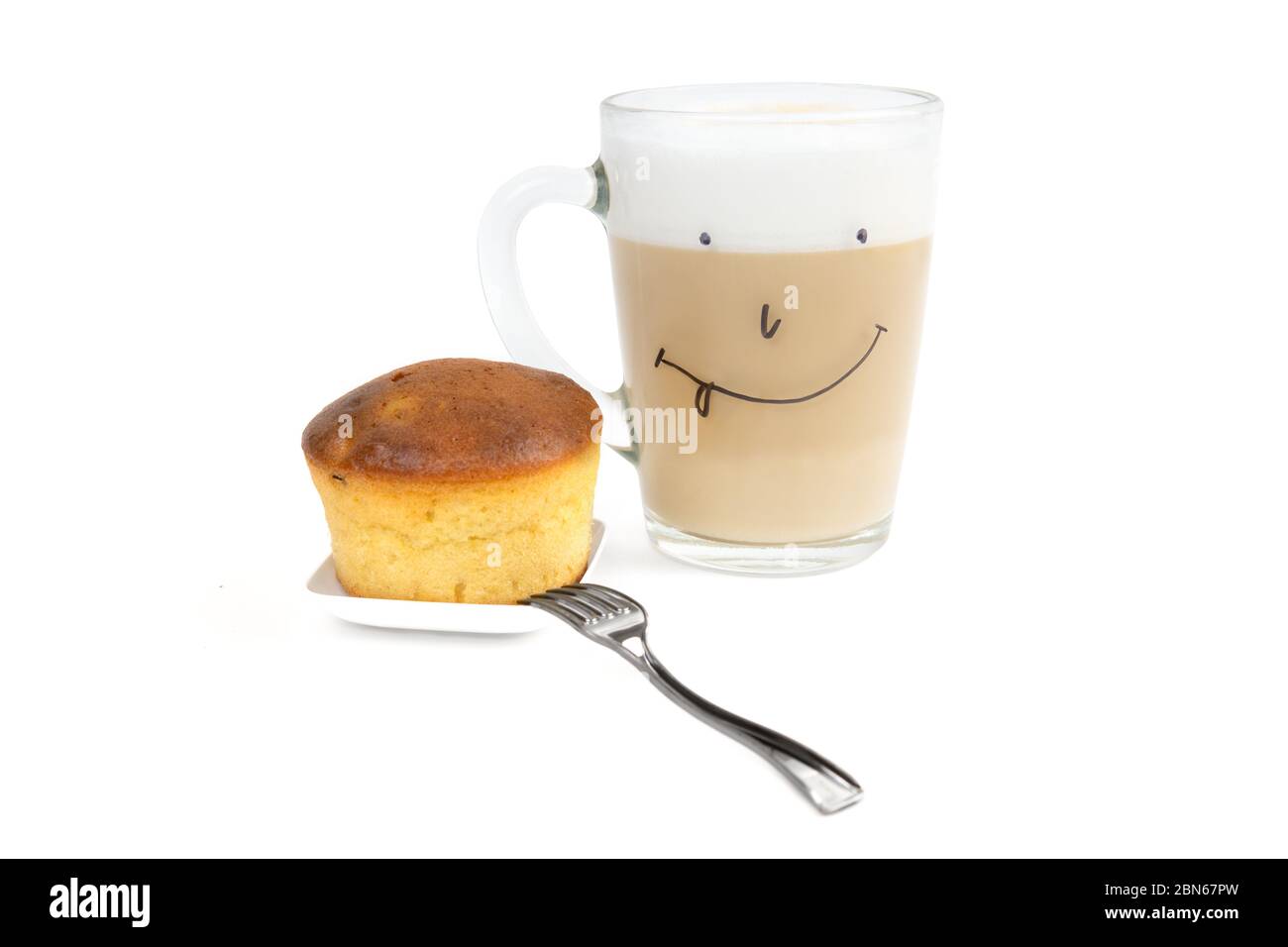 Cappuccino café avec mousse de lait riche dans une tasse en verre avec un visage drôle dessiné à la main, un cupcake maison et une petite fourchette isolée sur fond blanc. Banque D'Images
