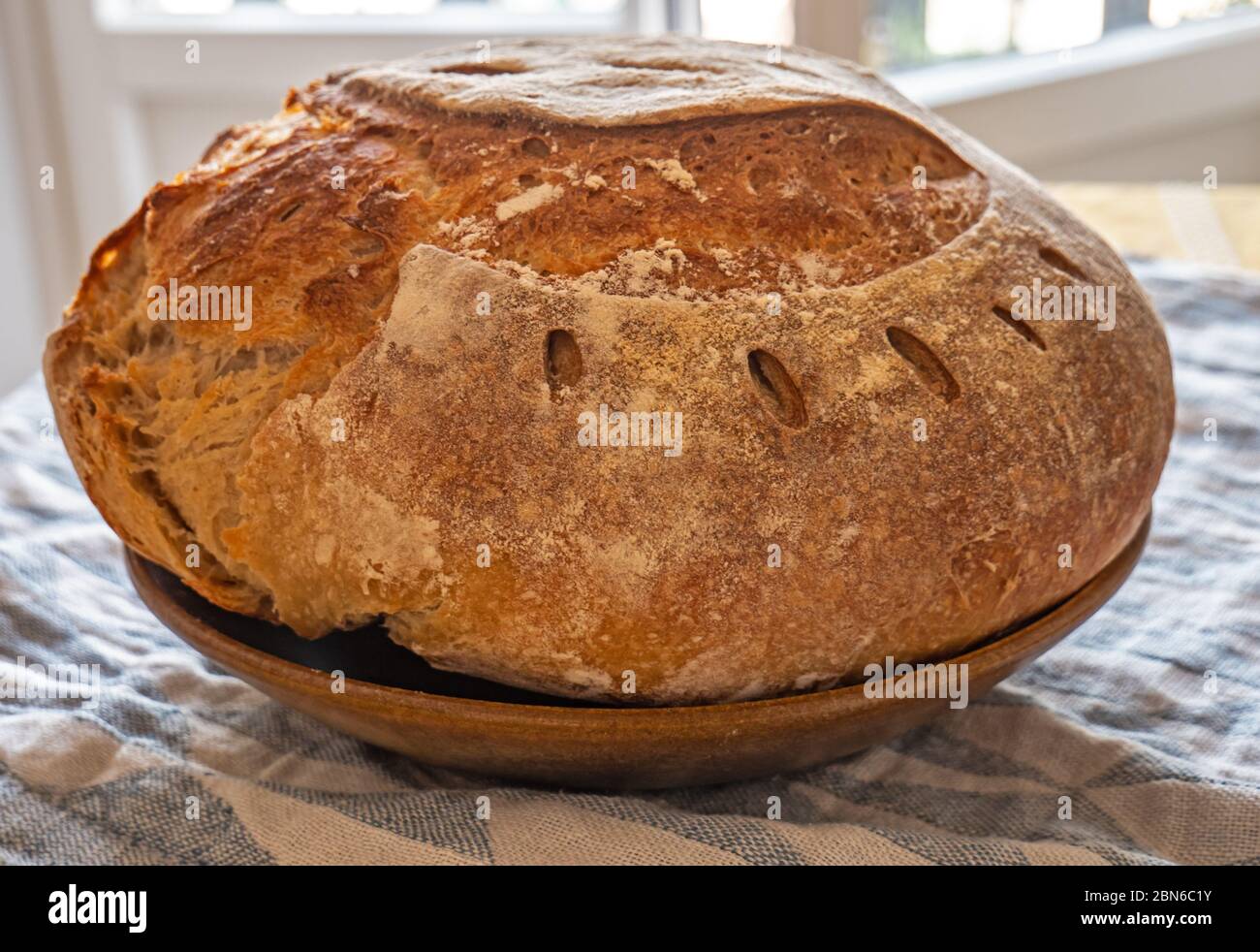 Pain Sourdough fraîchement préparé. Le pain de levain fraîchement préparé est installé sur une table recouverte de tissu dans une cuisine rustique. Le pain a une croûte dorée dehors. Banque D'Images