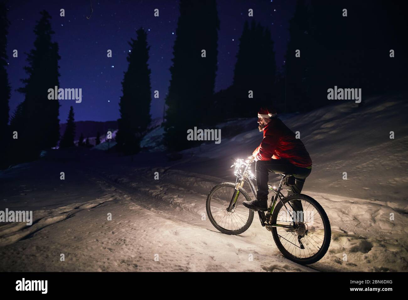 L'homme en rouge veste avec location et Noël hat à l'hiver la forêt enneigée dans les montagnes sous le ciel de nuit avec des étoiles Banque D'Images
