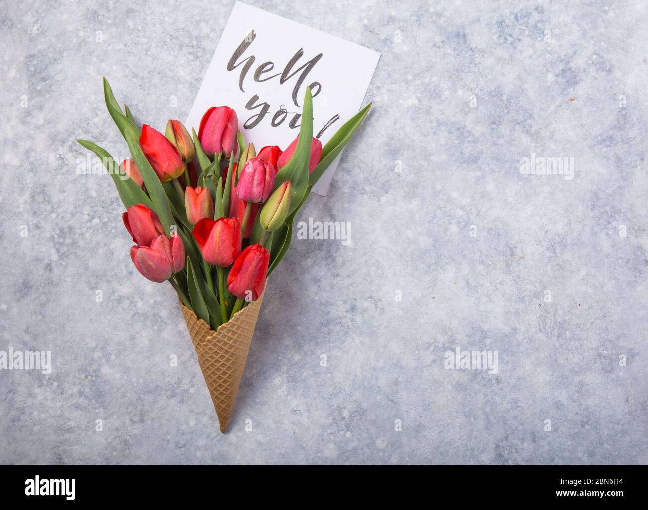 Rouge magnifiques tulipes dans un cône de gaufres de glace avec carte Bonjour sur un fond de béton. Idée conceptuelle d'un cadeau de fleur. Ambiance printanière Banque D'Images