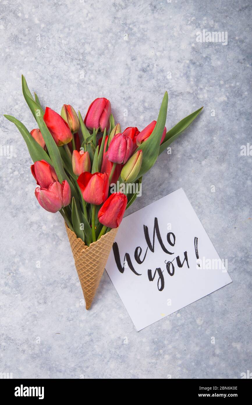 Rouge magnifiques tulipes dans un cône de gaufres de glace avec carte Bonjour sur un fond de béton. Idée conceptuelle d'un cadeau de fleur. Ambiance printanière Banque D'Images