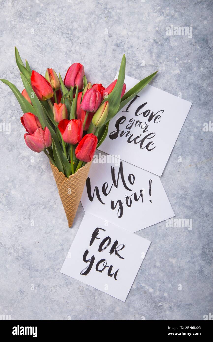 Rouge magnifiques tulipes dans un cône de gaufres de glace avec carte Bonjour sur un fond de béton. Idée conceptuelle d'un cadeau de fleur. Ambiance printanière Banque D'Images