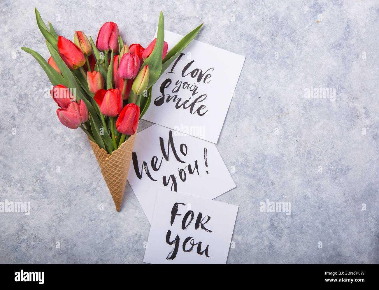 Rouge magnifiques tulipes dans un cône de gaufres de glace avec carte Bonjour sur un fond de béton. Idée conceptuelle d'un cadeau de fleur. Ambiance printanière Banque D'Images