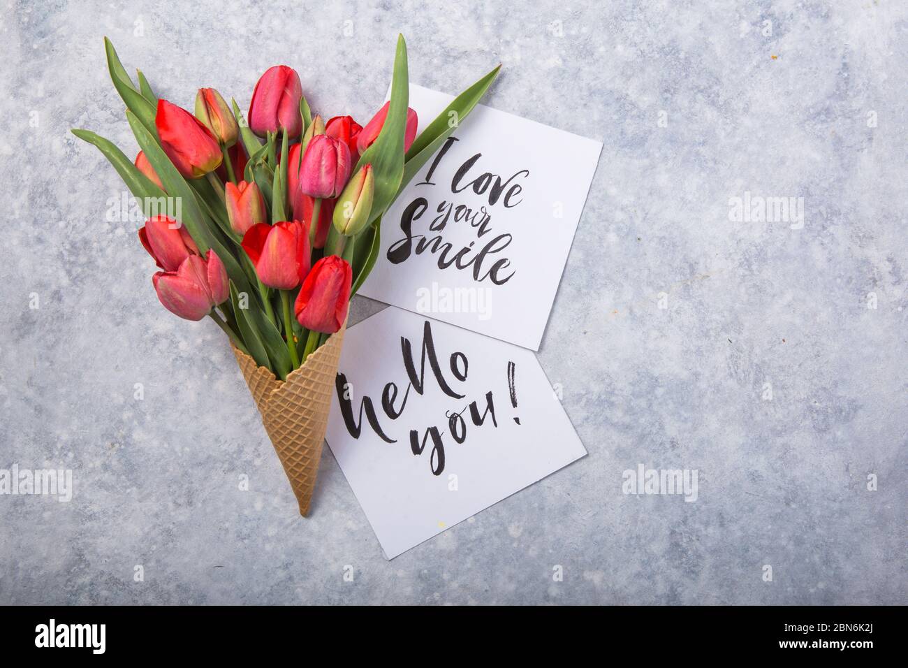 Rouge magnifiques tulipes dans un cône de gaufres de glace avec carte Bonjour sur un fond de béton. Idée conceptuelle d'un cadeau de fleur. Ambiance printanière Banque D'Images