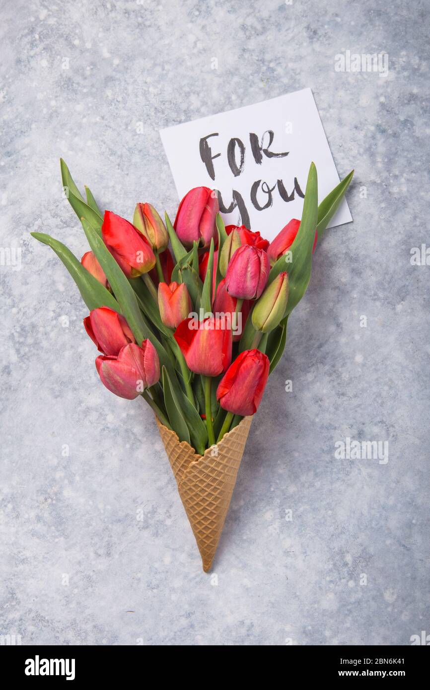 Rouge magnifiques tulipes dans un cône de gaufres de glace avec carte Bonjour sur un fond de béton. Idée conceptuelle d'un cadeau de fleur. Ambiance printanière Banque D'Images