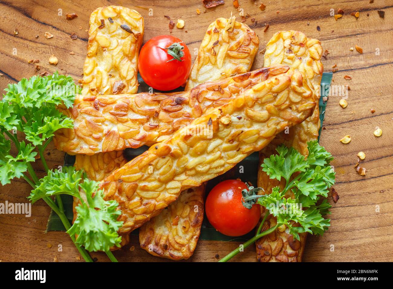 Tempeh (produit traditionnel de soja indonésien), tomates cerises et persil frits sur une surface en bois. Vue de dessus. Gros plan. Banque D'Images