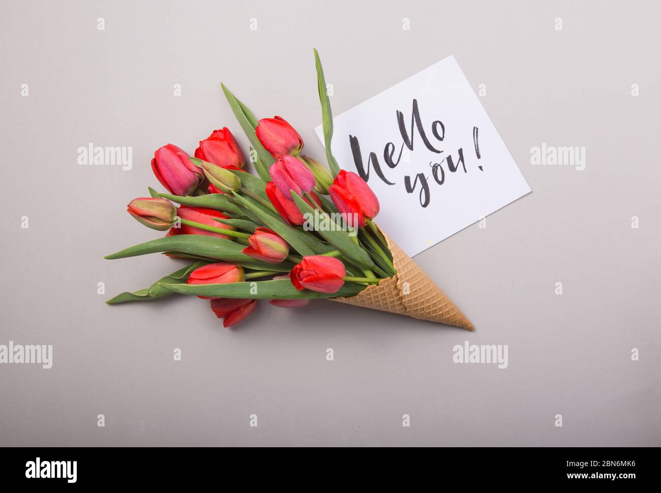 Rouge magnifiques tulipes dans un cône de gaufres de glace avec carte Bonjour sur un fond de béton. Idée conceptuelle d'un cadeau de fleur. Ambiance printanière Banque D'Images