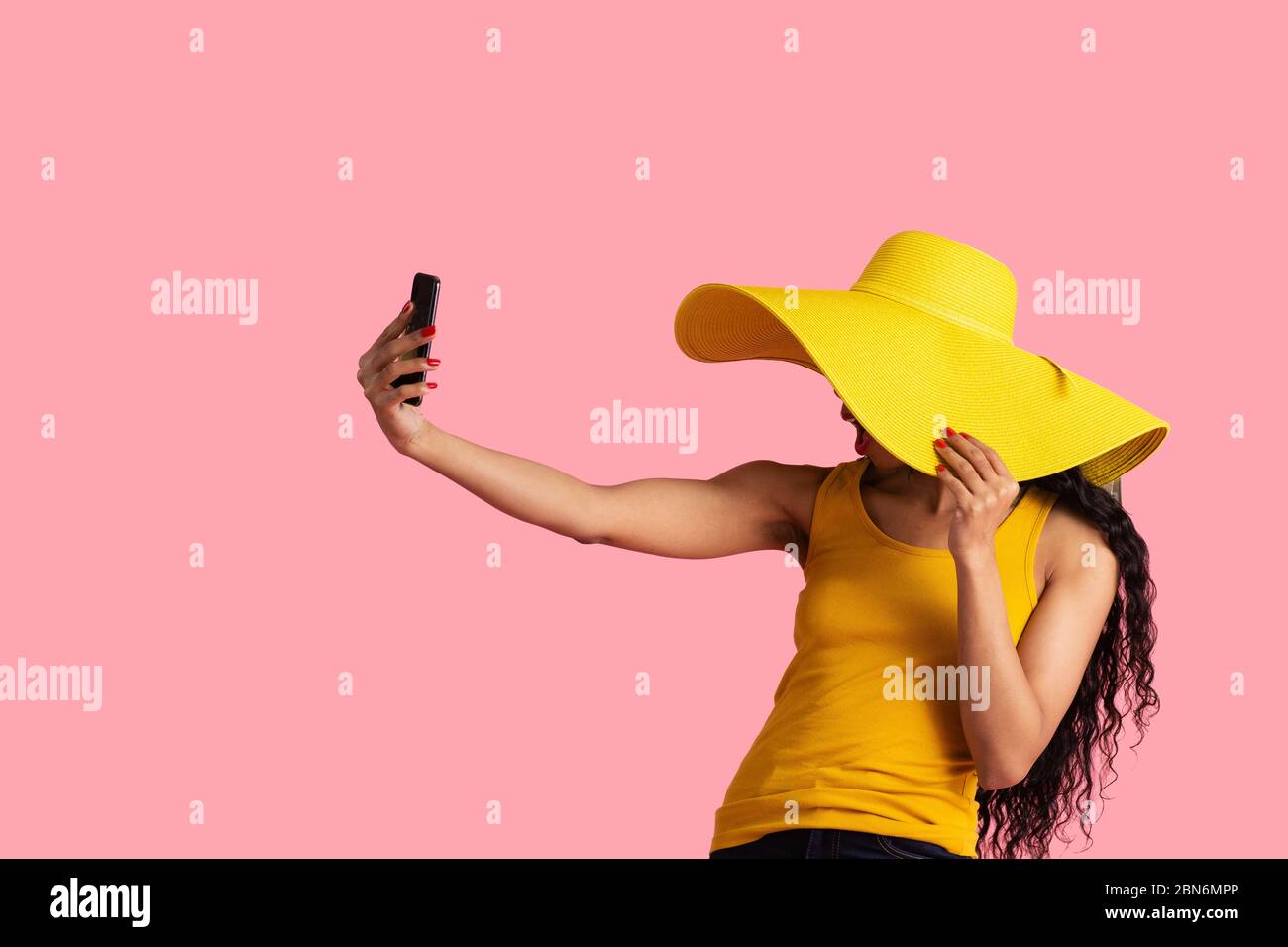 Portrait d'une jeune femme aux cheveux noirs et un grand chapeau jaune d'été prenant selfie avec son smartphone Banque D'Images