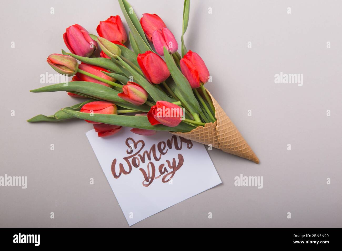 Rouge magnifiques tulipes dans un cône de gaufres de glace avec carte Bonjour sur un fond de béton. Idée conceptuelle d'un cadeau de fleur. Ambiance printanière Banque D'Images