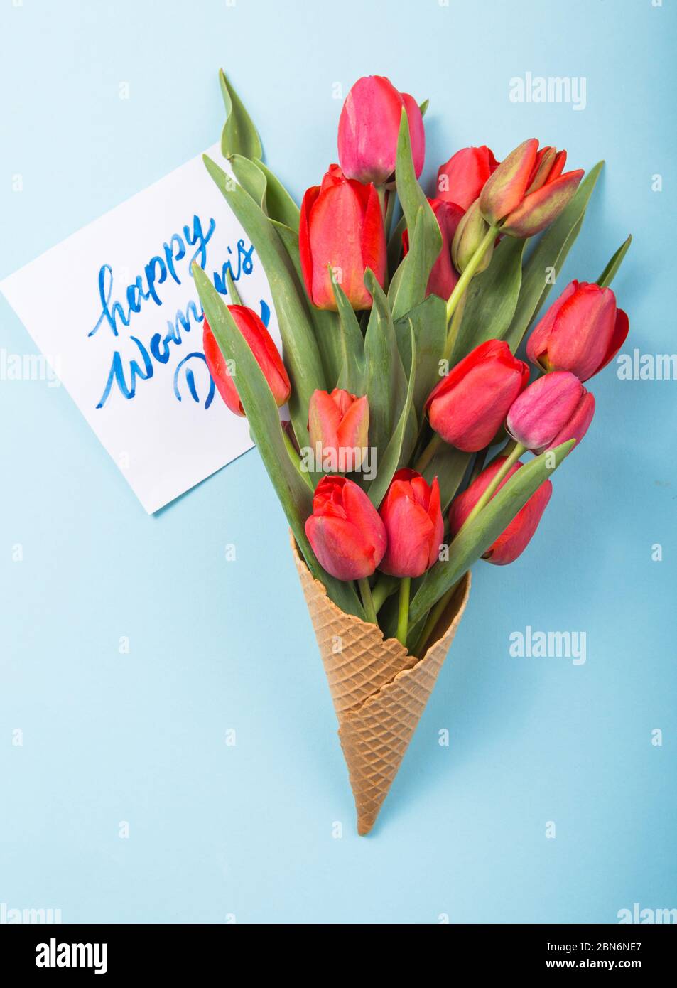 Rouge magnifiques tulipes dans un cône de gaufres de glace avec carte Womans Day sur un fond de béton. Idée conceptuelle d'un cadeau de fleur. Ambiance printanière Banque D'Images