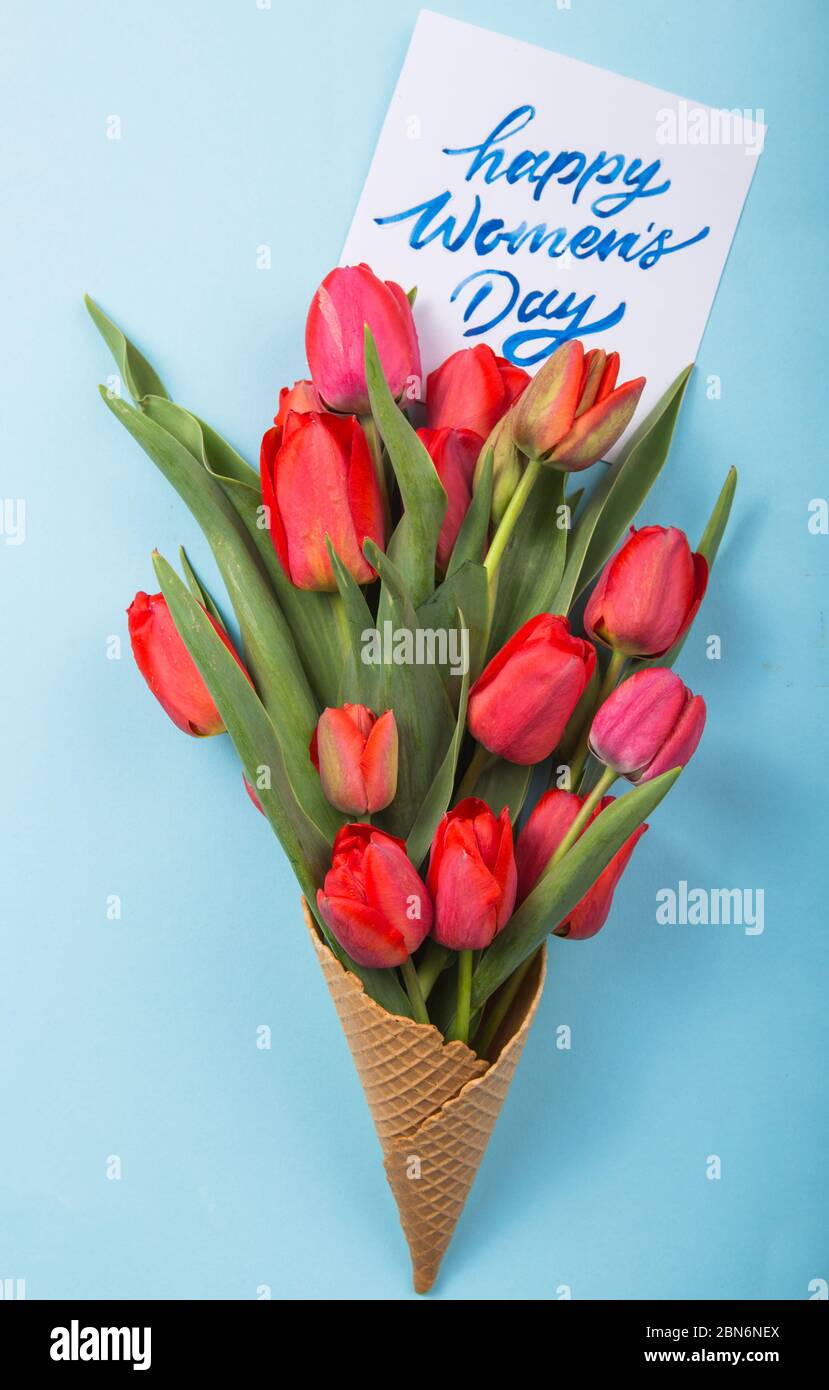 Rouge magnifiques tulipes dans un cône de gaufres de glace avec carte Womans Day sur un fond de béton. Idée conceptuelle d'un cadeau de fleur. Ambiance printanière Banque D'Images