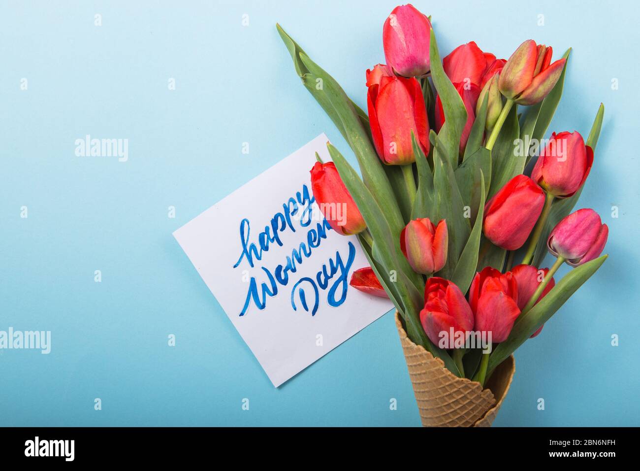 Rouge magnifiques tulipes dans un cône de gaufres de glace avec carte Womans Day sur un fond de béton. Idée conceptuelle d'un cadeau de fleur. Ambiance printanière Banque D'Images