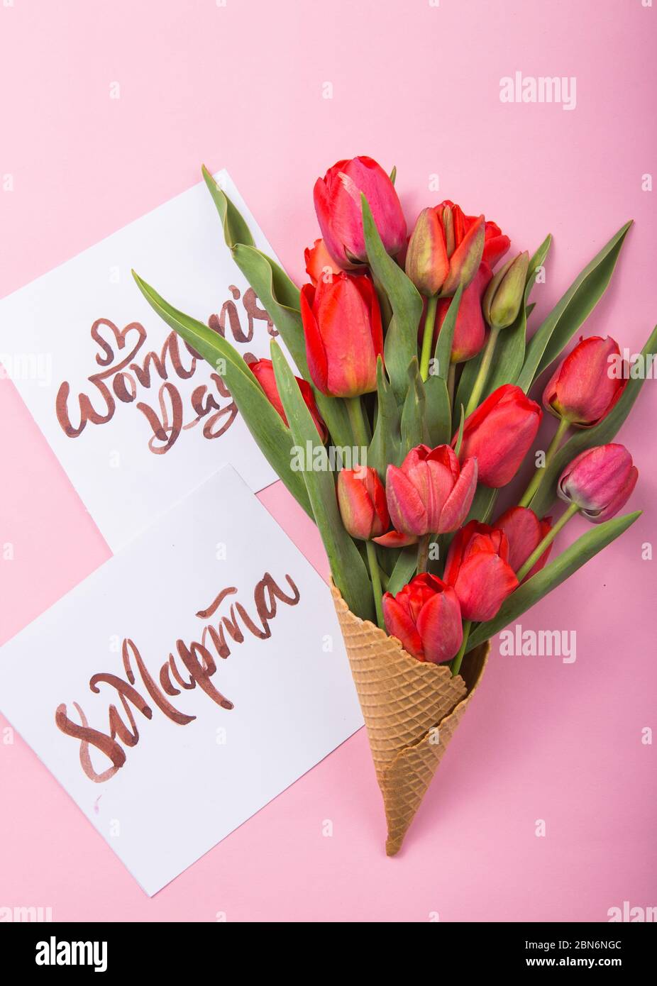 Rouge magnifique tulipes dans un cône de gaufre de glace avec carte Womans Day sur un fond de couleur. Idée conceptuelle d'un cadeau de fleur. Ambiance printanière Banque D'Images