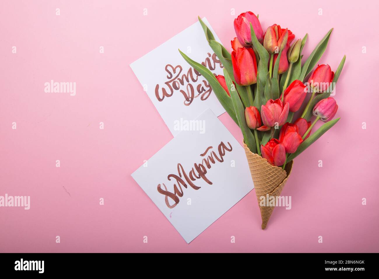 Rouge magnifique tulipes dans un cône de gaufre de glace avec carte Womans Day sur un fond de couleur. Idée conceptuelle d'un cadeau de fleur. Ambiance printanière Banque D'Images