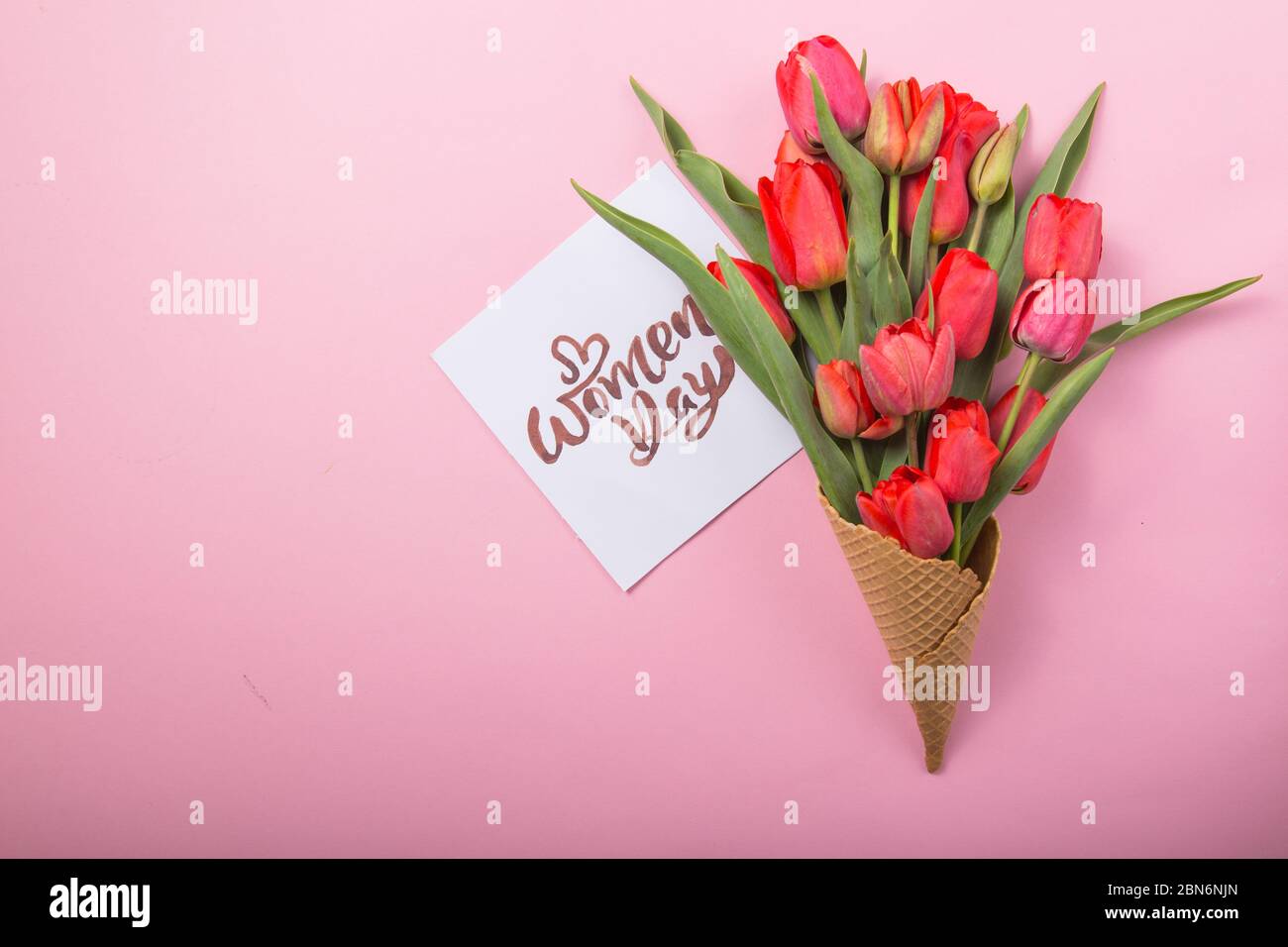 Rouge magnifique tulipes dans un cône de gaufre de glace avec carte Womans Day sur un fond de couleur. Idée conceptuelle d'un cadeau de fleur. Ambiance printanière Banque D'Images