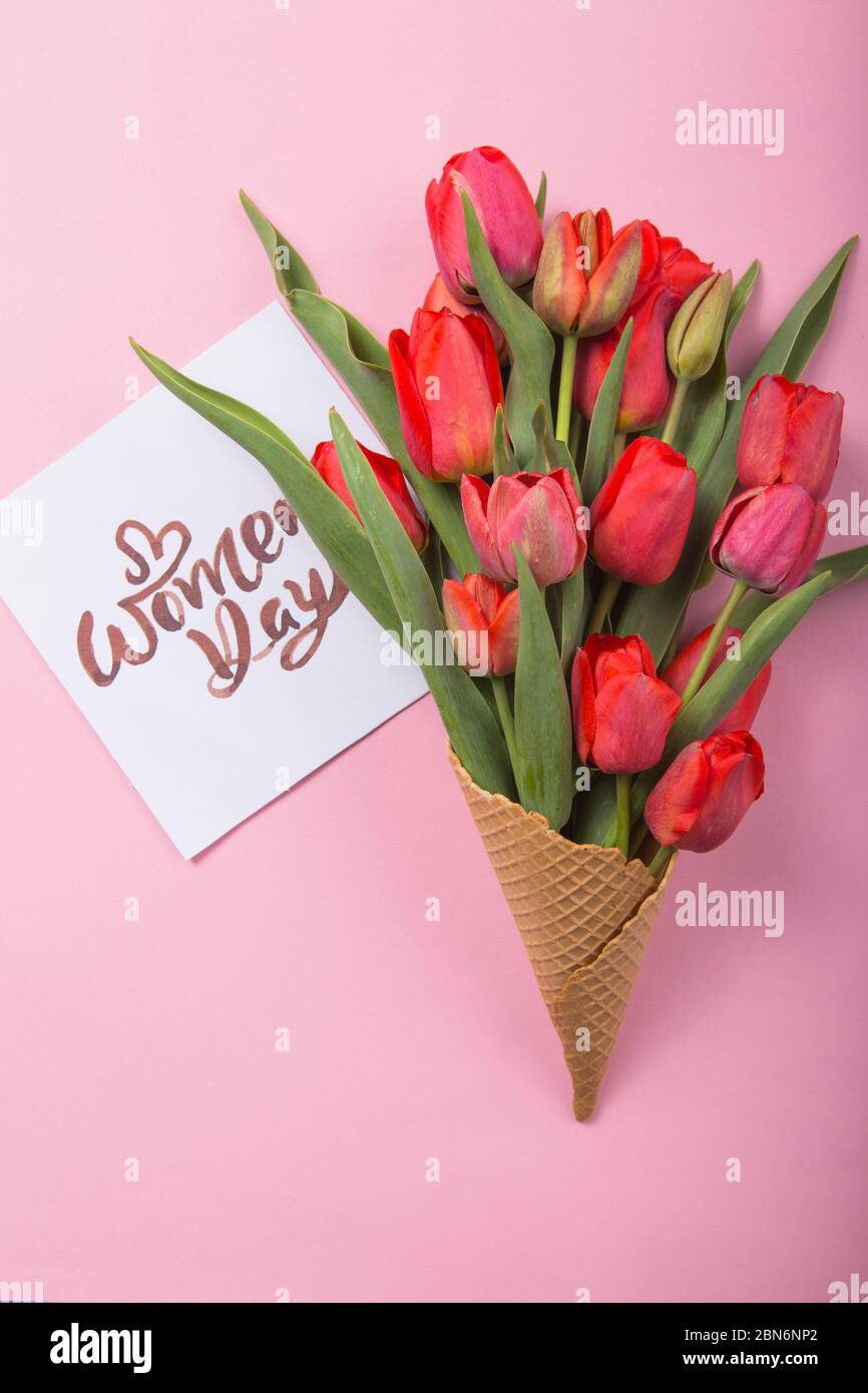Rouge magnifique tulipes dans un cône de gaufre de glace avec carte Womans Day sur un fond de couleur. Idée conceptuelle d'un cadeau de fleur. Ambiance printanière Banque D'Images