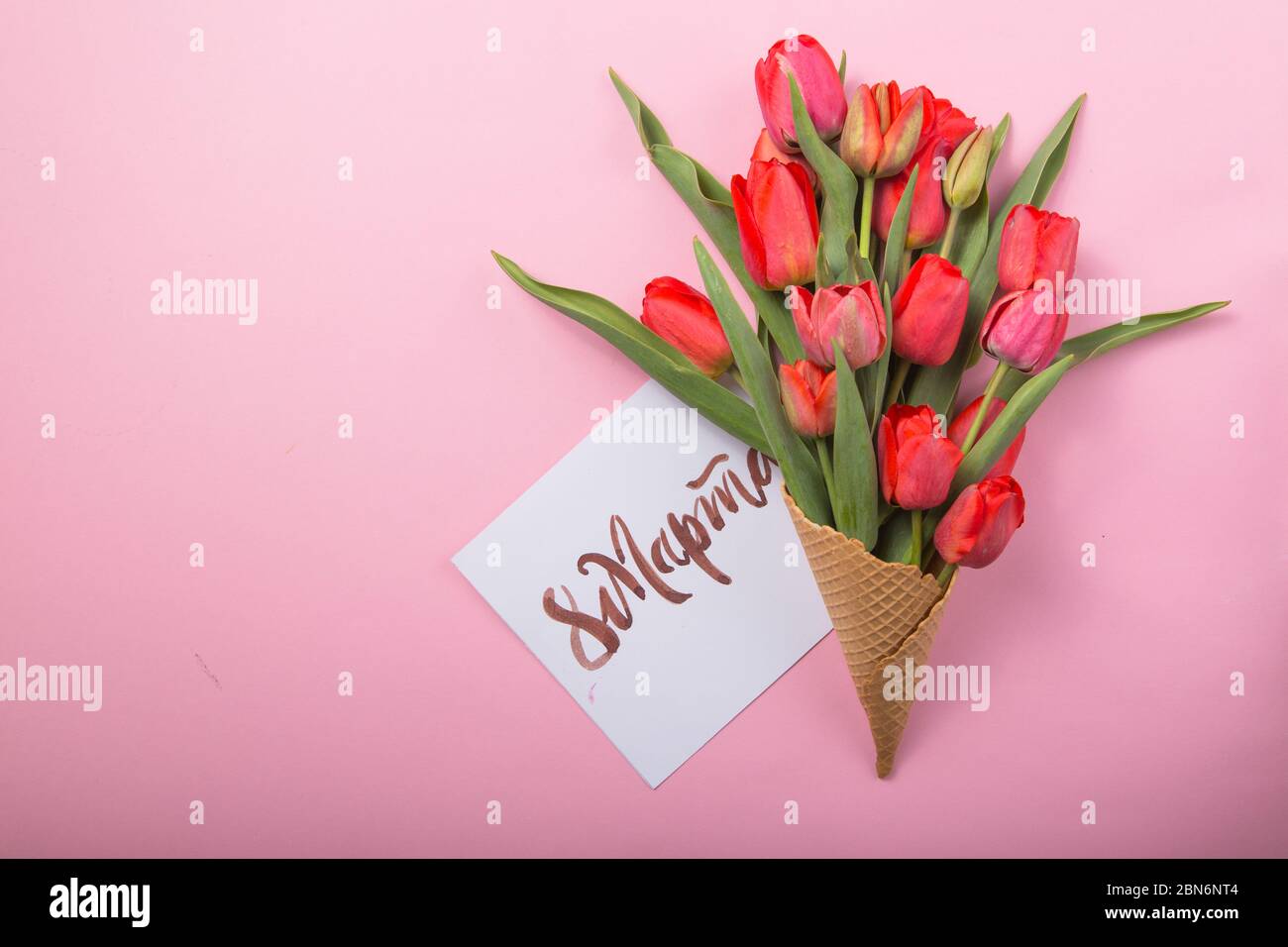 Rouge magnifique tulipes dans un cône de gaufre de glace avec carte Womans Day sur un fond de couleur. Idée conceptuelle d'un cadeau de fleur. Ambiance printanière Banque D'Images