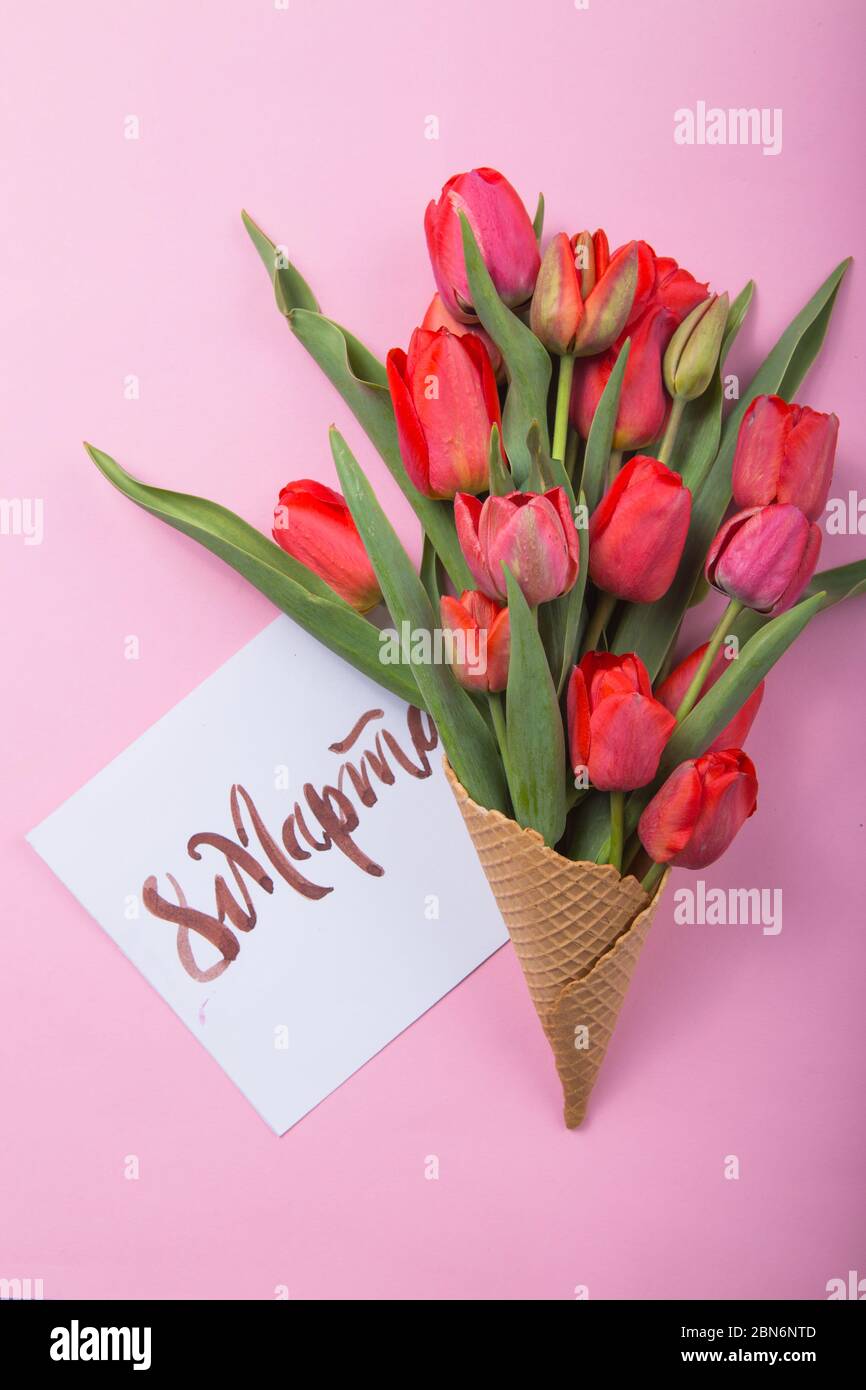 Rouge magnifique tulipes dans un cône de gaufre de glace avec carte Womans Day sur un fond de couleur. Idée conceptuelle d'un cadeau de fleur. Ambiance printanière Banque D'Images