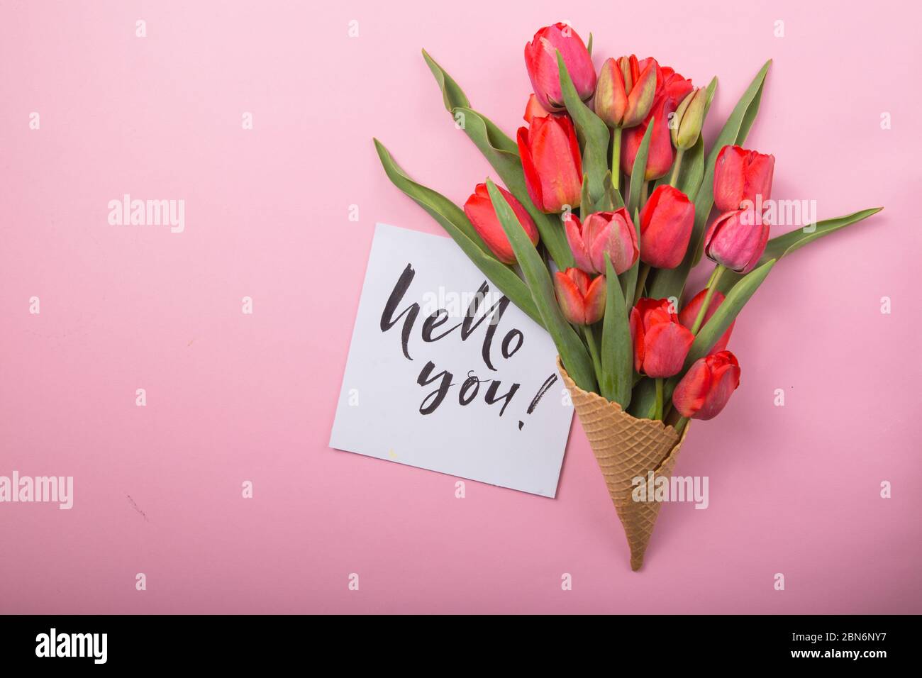 Rouge magnifiques tulipes dans un cône de gaufre de glace avec carte Bonjour sur un fond de couleur. Idée conceptuelle d'un cadeau de fleur. Ambiance printanière Banque D'Images