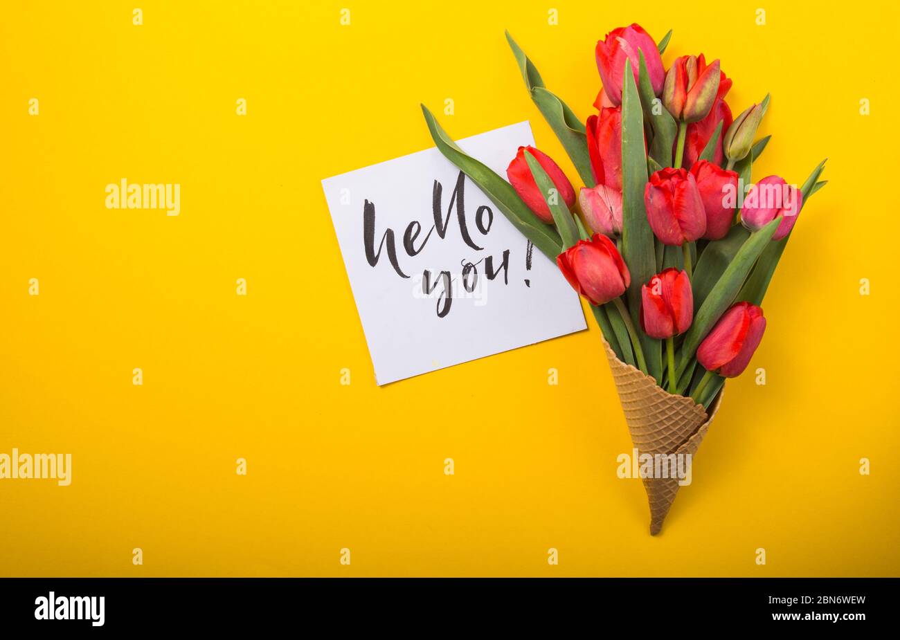 rouge magnifiques tulipes dans un cône de gaufre de glace avec carte d'encre un fond jaune. Idée conceptuelle d'un cadeau de fleur. Ambiance printanière Banque D'Images