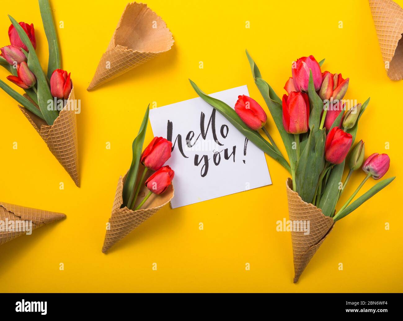 rouge magnifiques tulipes dans un cône de gaufre de glace avec carte d'encre un fond jaune. Idée conceptuelle d'un cadeau de fleur. Ambiance printanière Banque D'Images