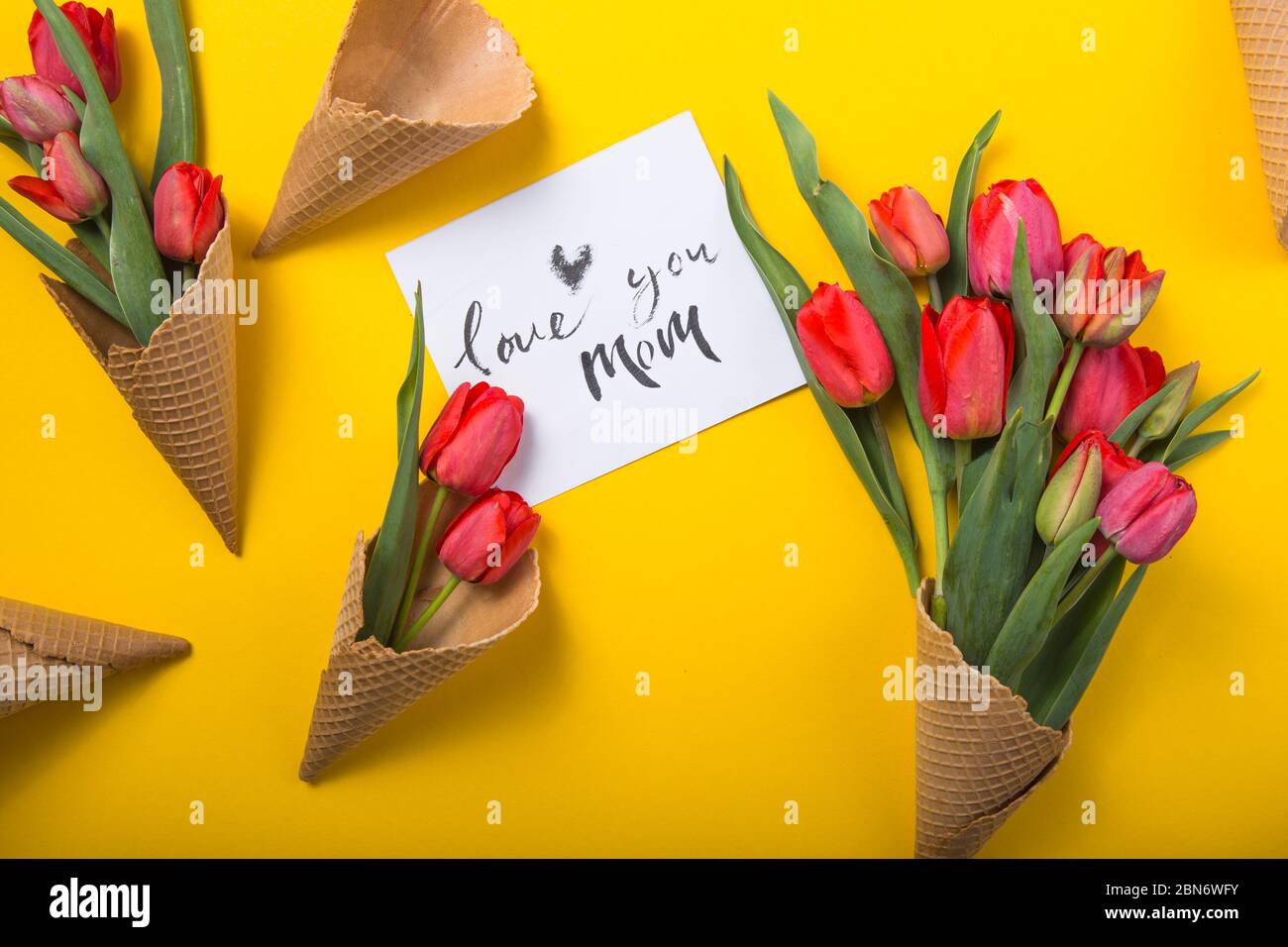 rouge magnifiques tulipes dans un cône de gaufre de glace avec carte d'encre un fond jaune. Idée conceptuelle d'un cadeau de fleur. Ambiance printanière Banque D'Images