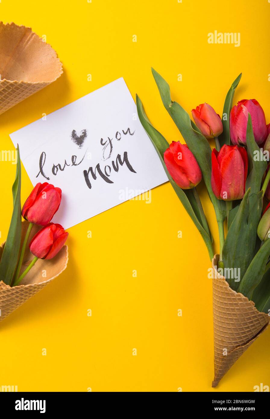 rouge magnifiques tulipes dans un cône de gaufre de glace avec carte d'encre un fond jaune. Idée conceptuelle d'un cadeau de fleur. Ambiance printanière Banque D'Images