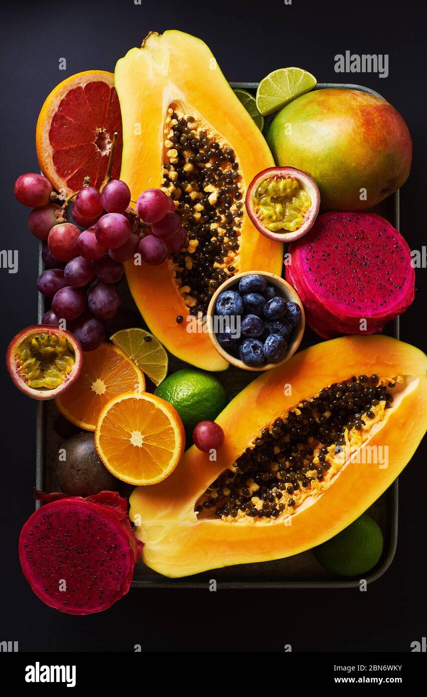 Les fruits tropicaux sont plats avec de la mangue, de la papaye, de la pitahaya, des fruits de la passion, du raisin, des limes et des ananas. Table avec ingrédients pour les en-cas d'été sur b foncé Banque D'Images