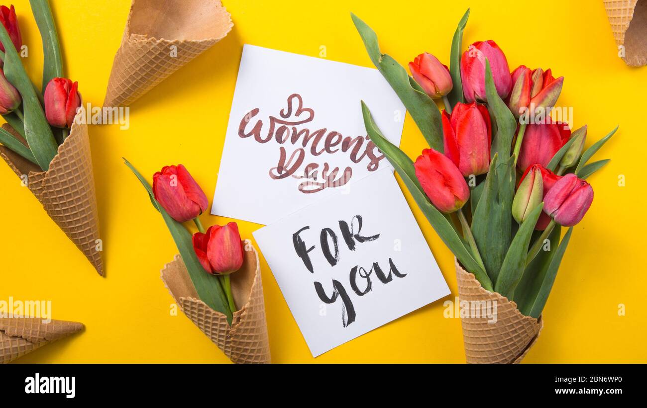rouge magnifiques tulipes dans un cône de gaufre de glace avec carte d'encre sur un fond jaune. Idée conceptuelle d'un cadeau de fleur. Ambiance printanière Banque D'Images