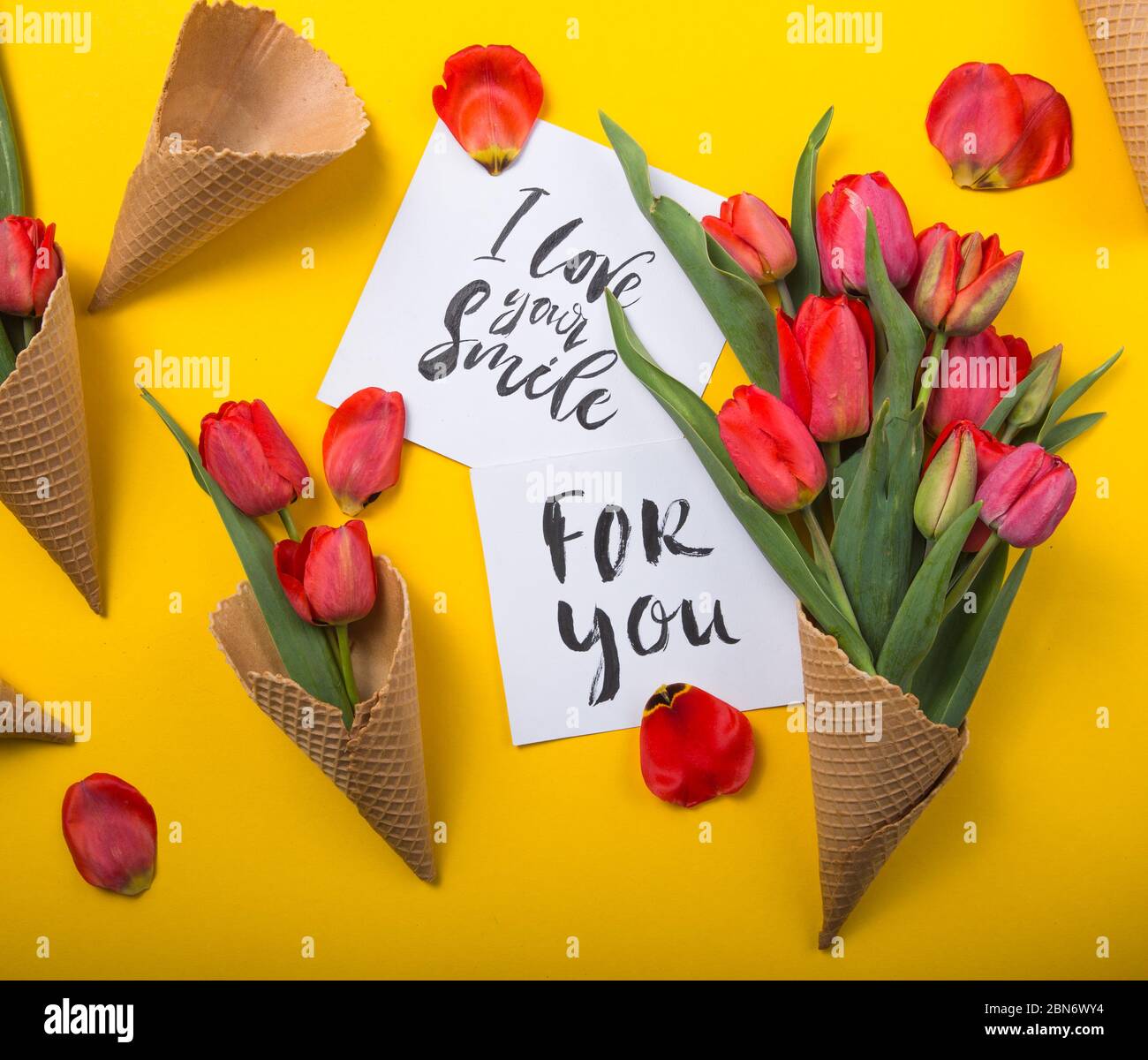 rouge magnifiques tulipes dans un cône de gaufre de glace avec carte d'encre sur un fond jaune. Idée conceptuelle d'un cadeau de fleur. Ambiance printanière Banque D'Images