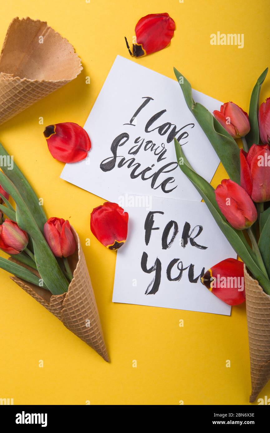 rouge magnifiques tulipes dans un cône de gaufre de glace avec carte d'encre sur un fond jaune. Idée conceptuelle d'un cadeau de fleur. Ambiance printanière Banque D'Images