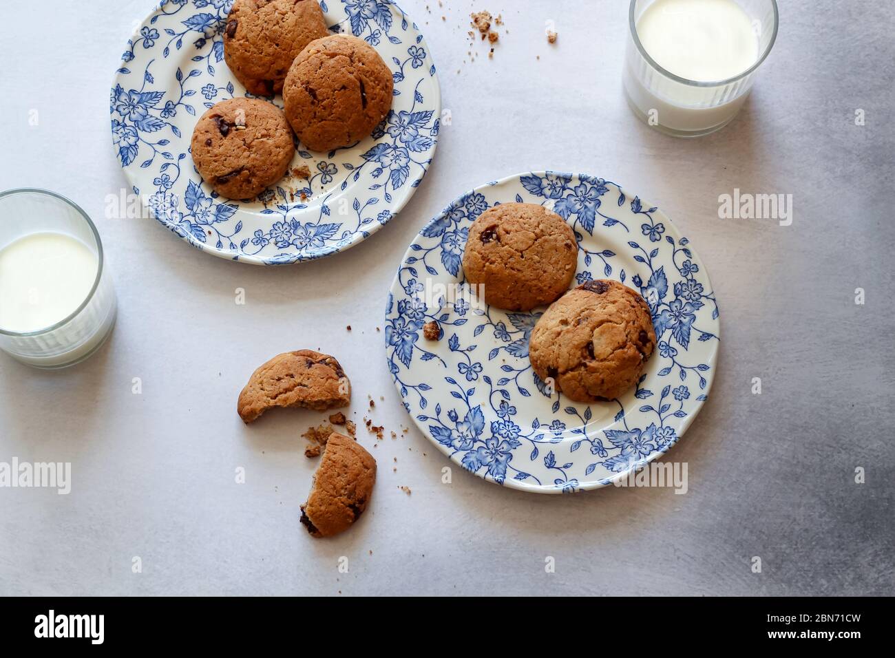 Biscuits aux pépites de chocolat sur des assiettes bleues et 2 verres de lait sur une table de cuisine grise Banque D'Images