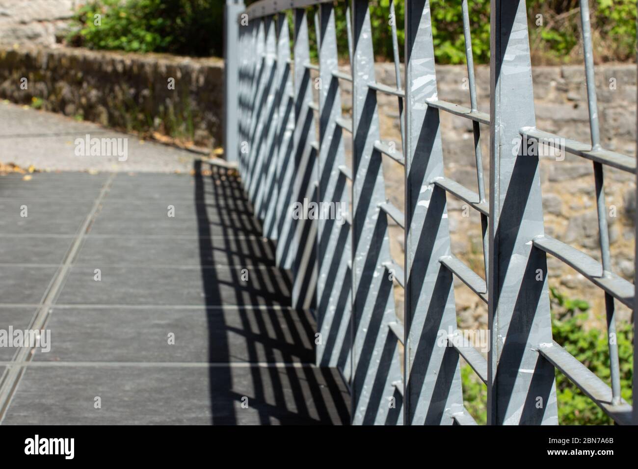 Vue inclinée d'une rambarde métallique sur un pont qui projette des ombres avec des murs en pierre naturelle en arrière-plan, mise au point au premier plan Banque D'Images