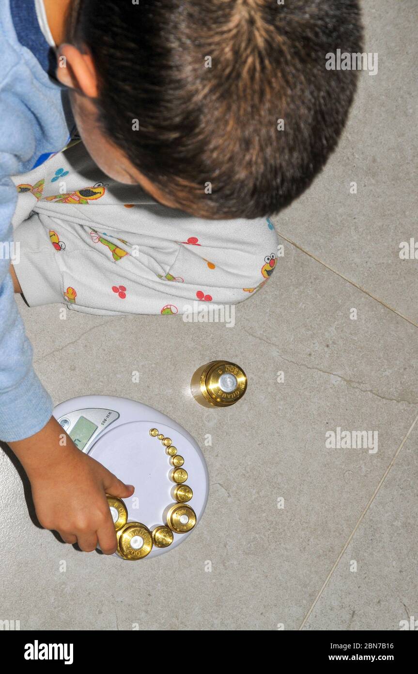 Jeune garçon de 5 ans pratique l'arithmétique à l'aide de poids de précision et d'une échelle numérique Banque D'Images