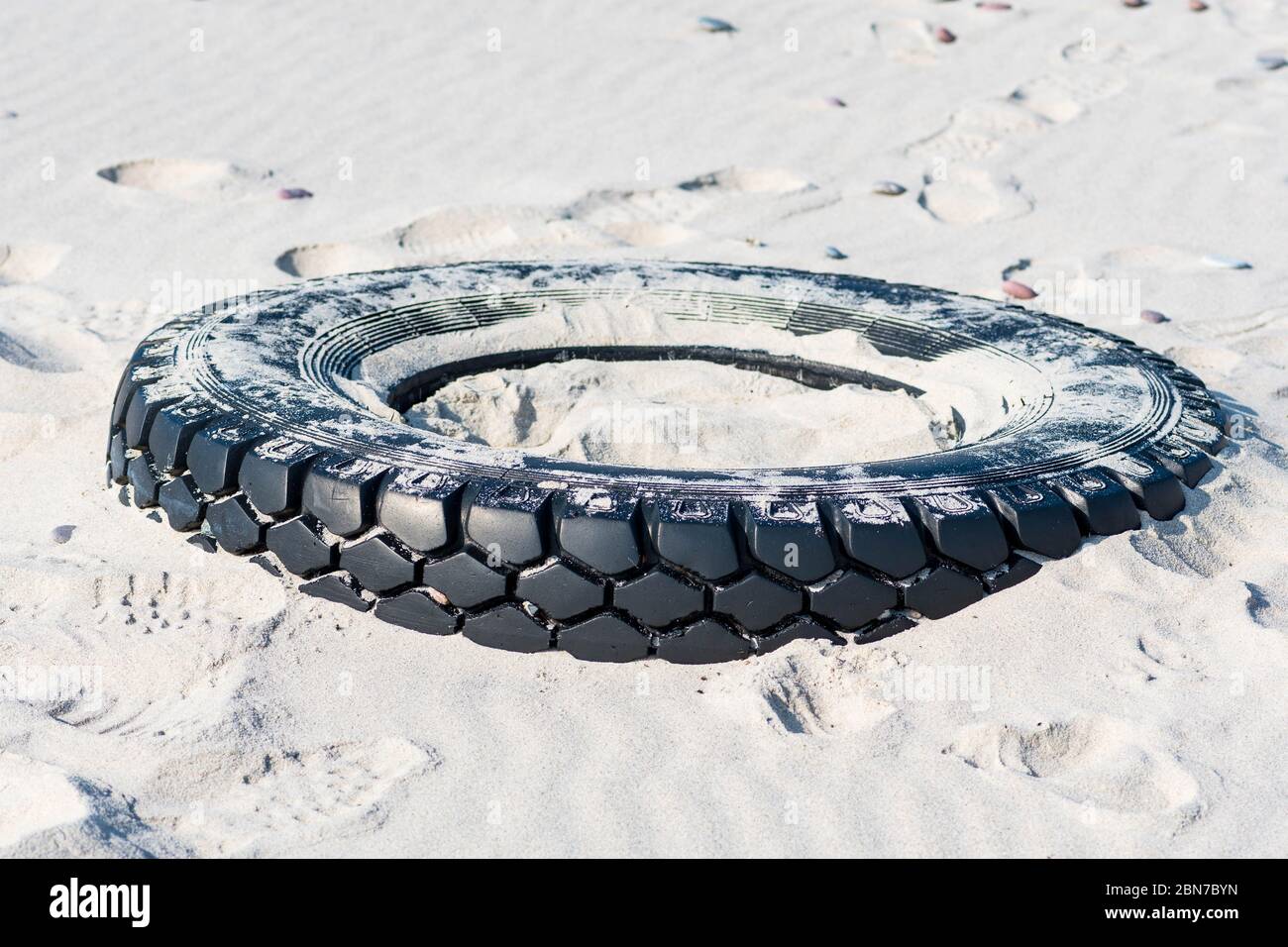 Grand pneu en caoutchouc noir laissé sur une plage de sable, concept de pollution de l'environnement Banque D'Images