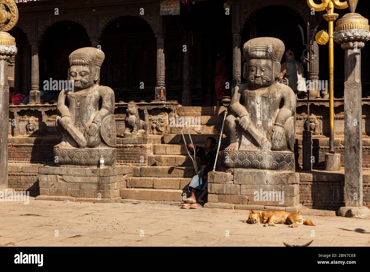 Bhaktapur, Népal - 15 novembre 2016 : entrée du temple hindou de Dattatraya. Un chien rouge dort près de l'entrée. Un homme avec des béquilles est assis sur les marches o Banque D'Images