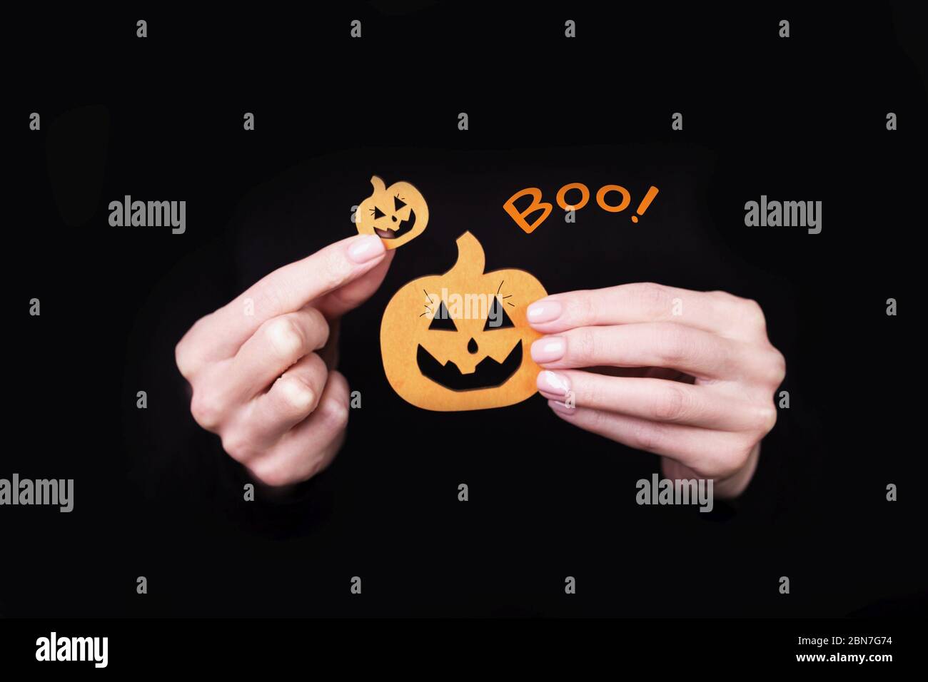 Les mains des femmes portant des petits citrouilles drôles sur fond noir. Carte d'Halloween avec inscription Boo Banque D'Images