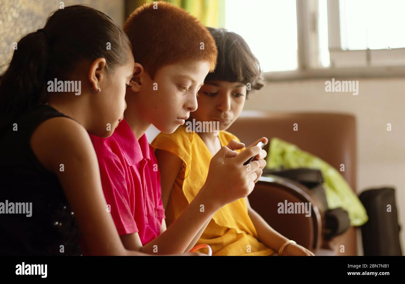 Trois enfants ou frères et sœurs de différentes ethnies qui jouent sur le mobile à la maison - concept de l'addiction de jeux vidéo mobiles pour enfants, en utilisant la technologie Banque D'Images