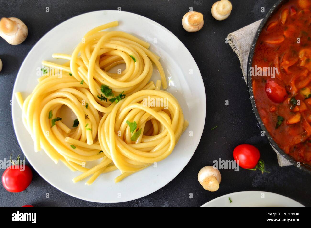 Pâtes dans une assiette blanche sur fond sombre. Spaghetti appétissants avec tomates et champignons. Vue de dessus de la nourriture. Banque D'Images