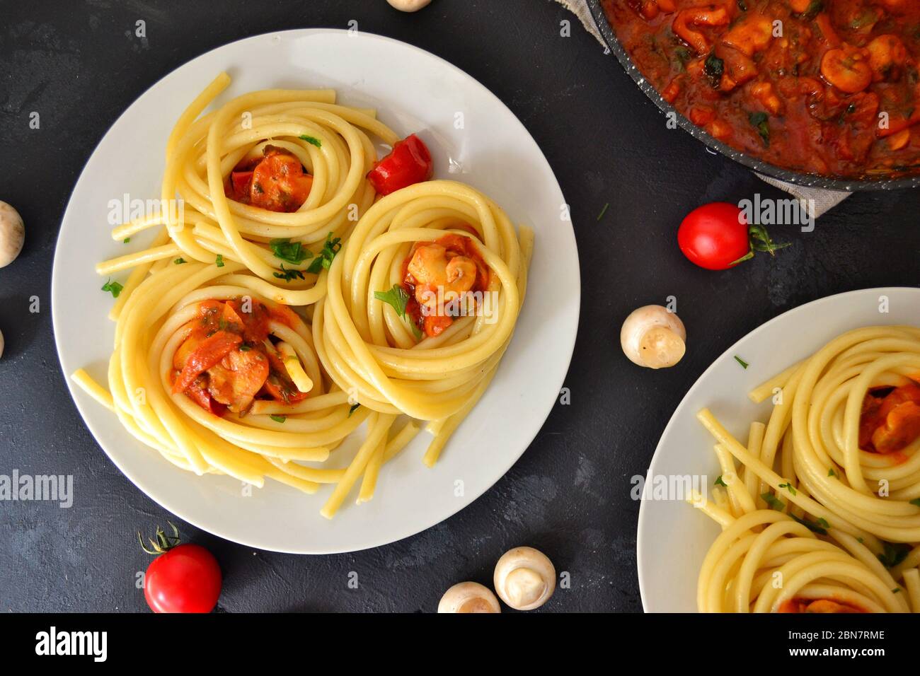 Pâtes dans une assiette blanche sur fond sombre. Spaghetti appétissants avec tomates et champignons. Vue de dessus de la nourriture. Banque D'Images