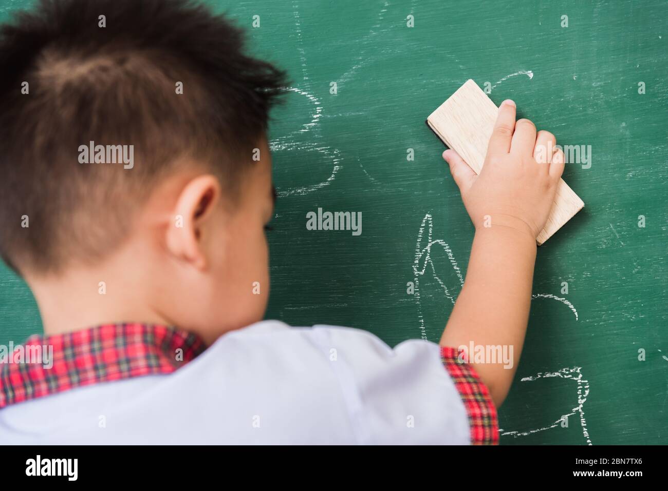 Rentrée des classes. Arrière de l'asiatique mignon petit enfant garçon  maternelle dans l'uniforme d'étudiant essuyant propre ou effacer la craie  sur vert école tableau noir W Photo Stock - Alamy