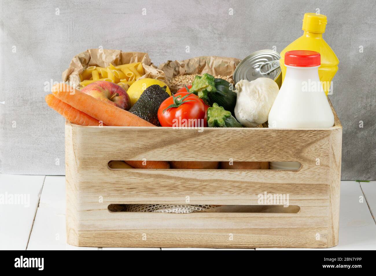 Don de nourriture boîte en bois avec légumes, fruits, pâtes, huile, lait et conserves. Isolé sur fond gris. Banque D'Images