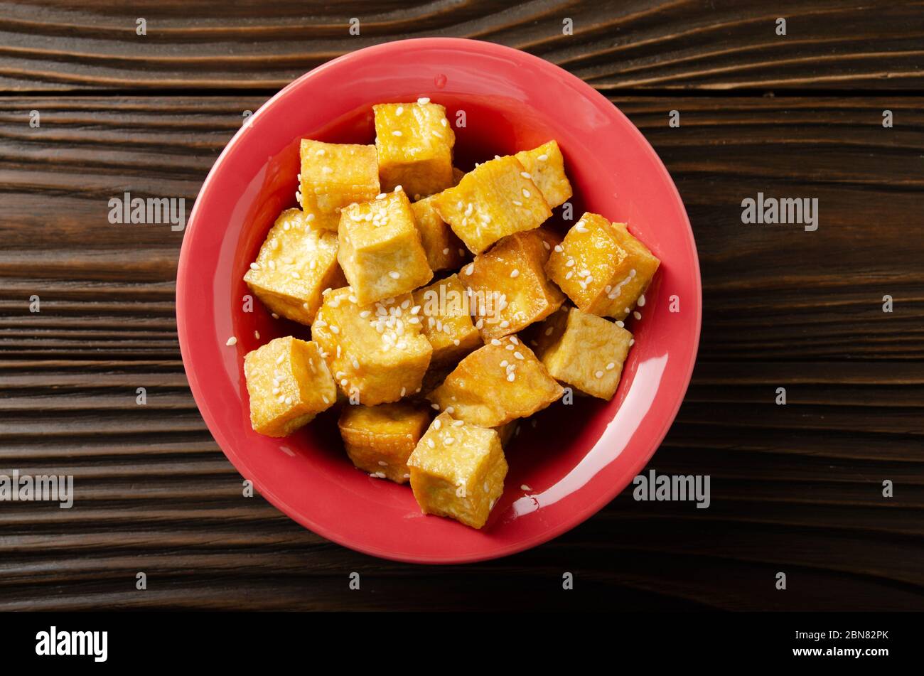 Plat posez la vue rapprochée sur des cubes de tofu frits croustillants et sautés avec ciboulette dans un plat en argile sur une table de cuisine en bois Banque D'Images