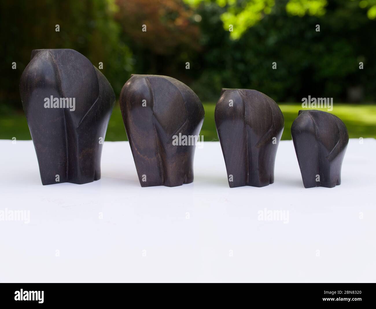 Quatre éléphants africains en bois sculptés sur une surface blanche sur fond vert Banque D'Images