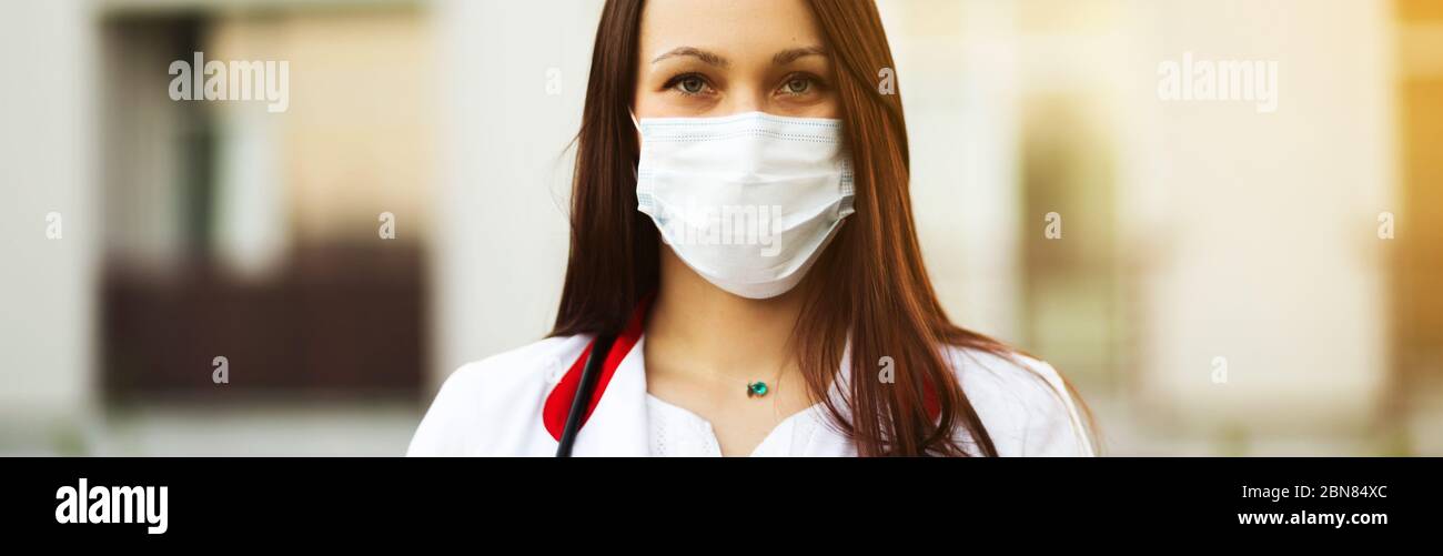Jeune femme médecin en masque chirurgical et écouteurs en extérieur bannière Banque D'Images