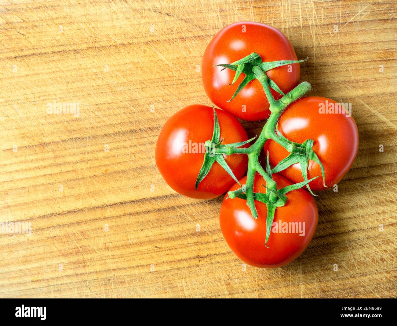 Quatre tomates rouges mûres sur la vigne sur une planche à découper en bois avec espace pour copier Banque D'Images