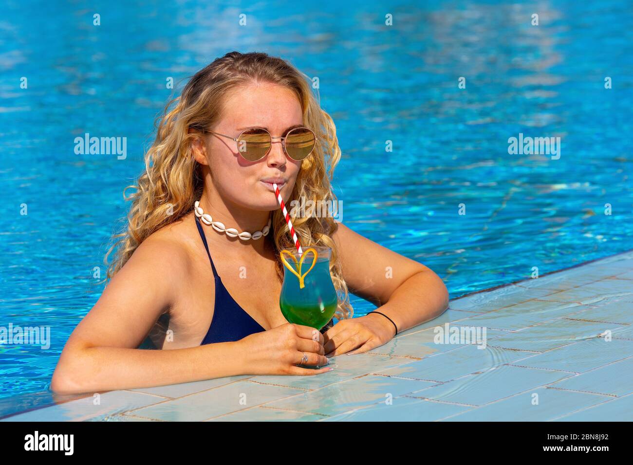 Jeune femme de race blanche qui boit un cocktail à la piscine Banque D'Images