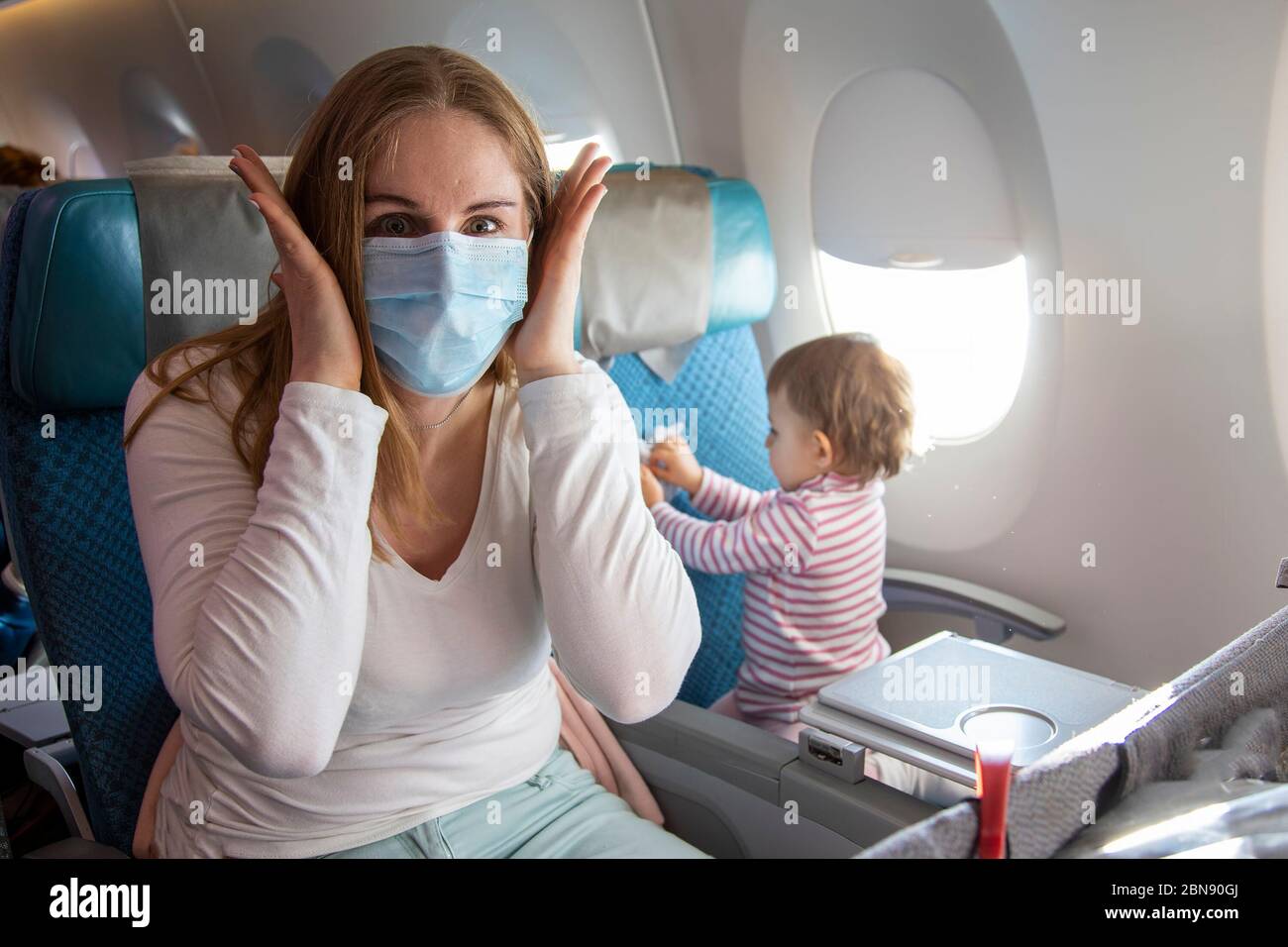 concept panique coronavirus covid-19..une jeune mère est assise dans un fauteuil d'avion dans un masque respiratoire médical avec un visage effrayé qui se hait à la caméra Banque D'Images